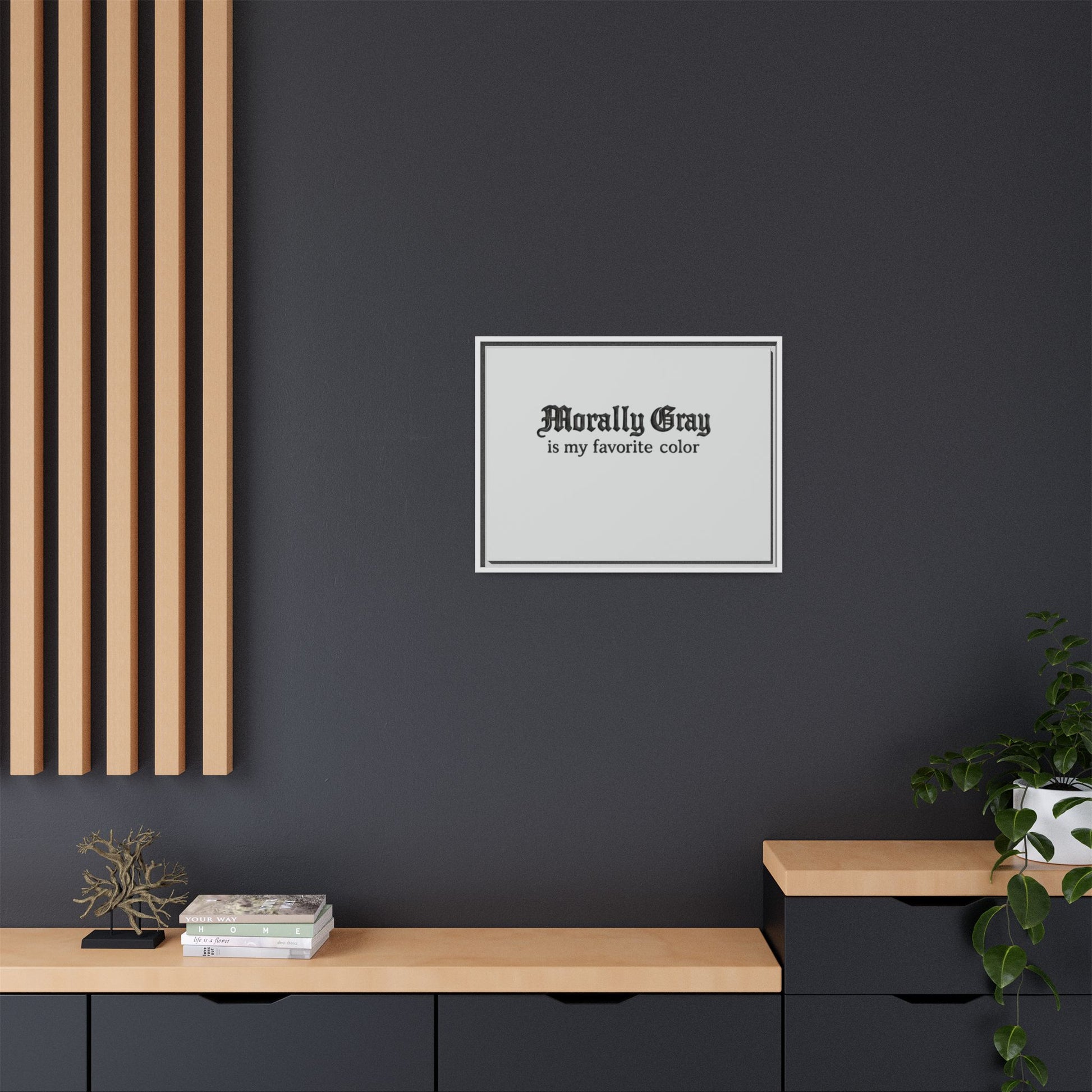 Framed wall art with the phrase "Morally Gray is my favorite color" displayed on a dark gray wall above a modern black and light wood shelf with plants and books, Unknown Product