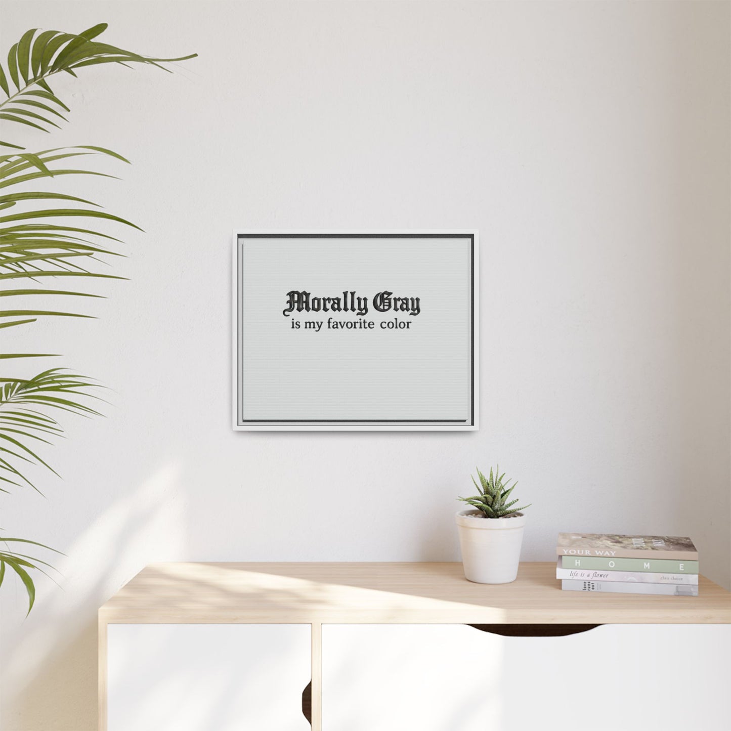 Minimalist framed wall art with gothic-style text reading "Morally Gray is my favorite color" above a wooden surface with a small potted succulent and stacked books featuring the Unknown Product.