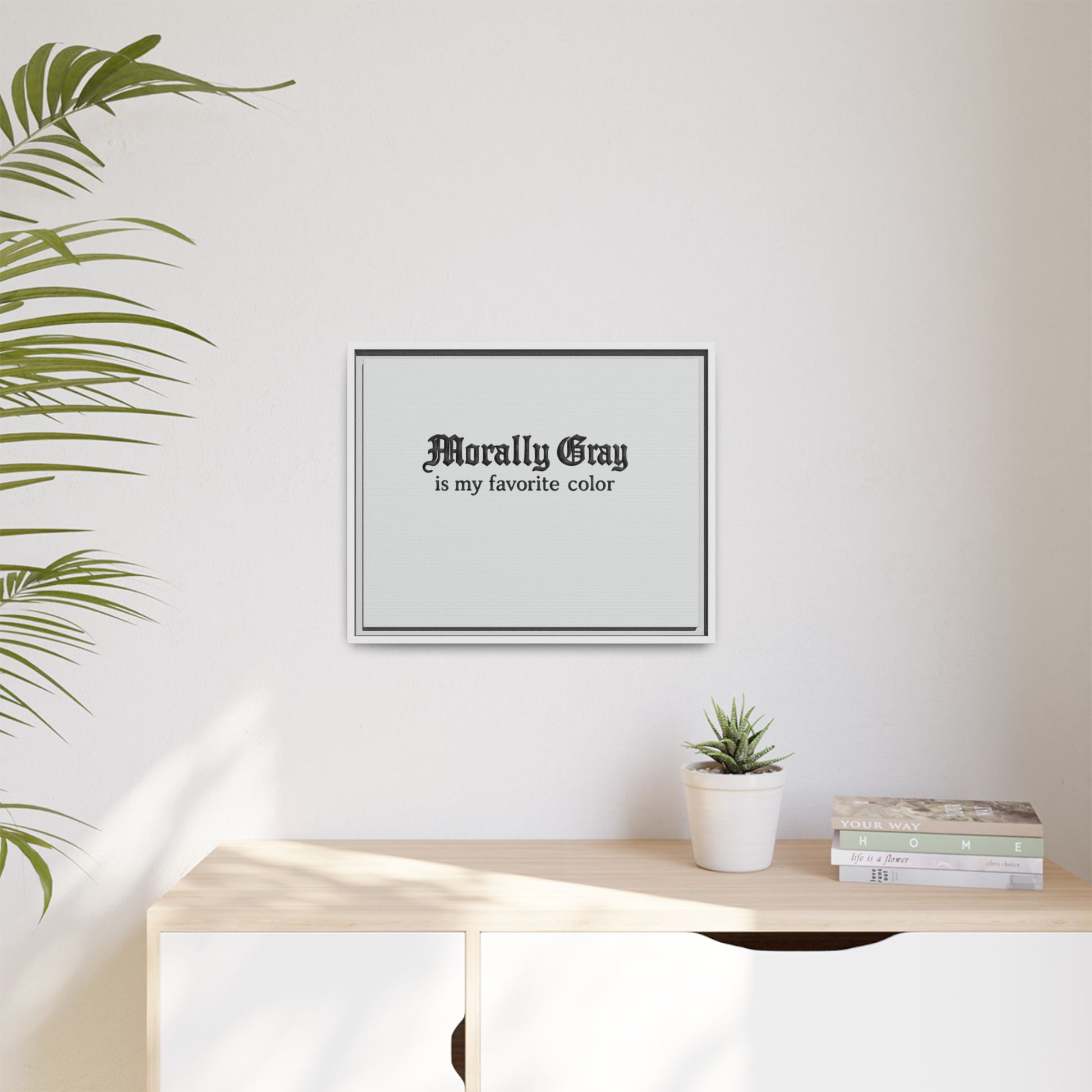 Minimalist framed wall art with gothic-style text reading "Morally Gray is my favorite color" above a wooden surface with a small potted succulent and stacked books featuring the Unknown Product.