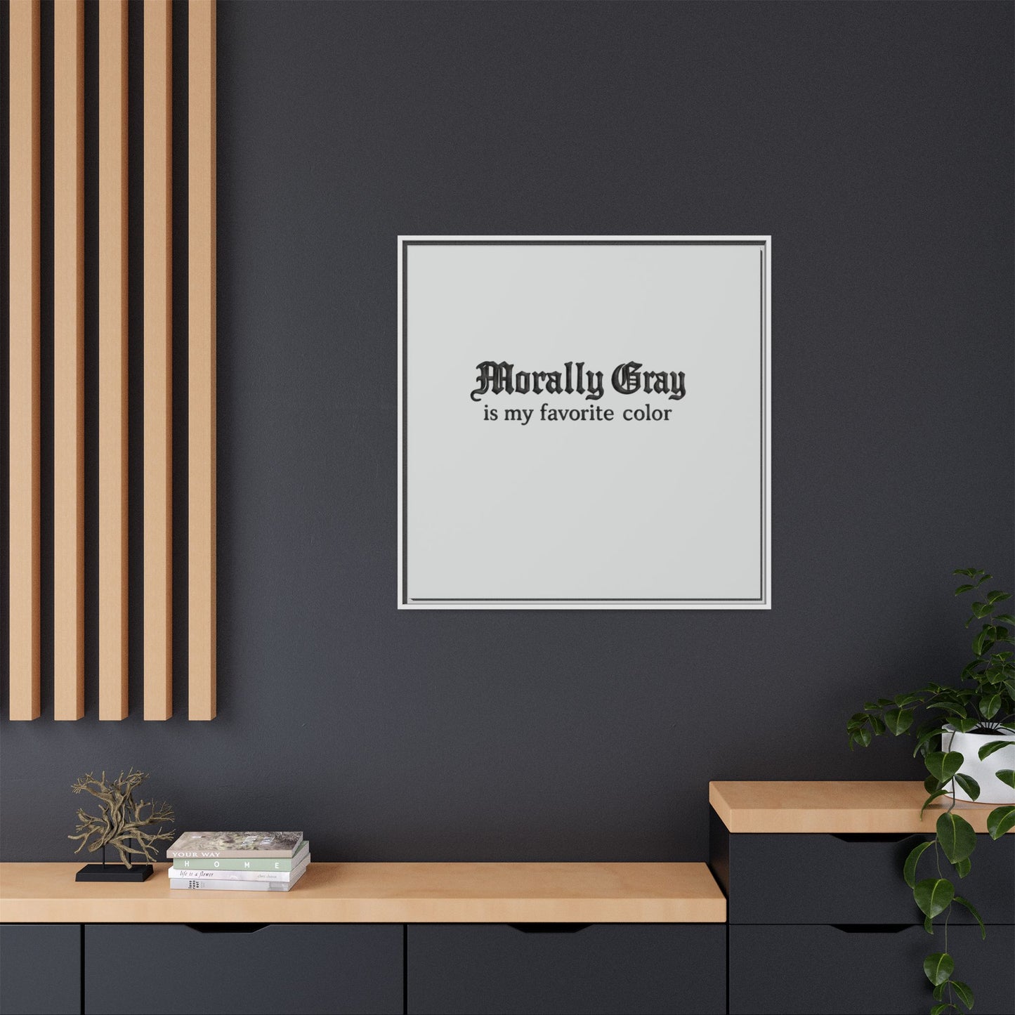 Square wall art with black Old English font saying "Morally Gray is my favorite color" on a light gray background in a modern minimalist room featuring black walls, wooden shelves, and green plants, featuring Unknown Product.