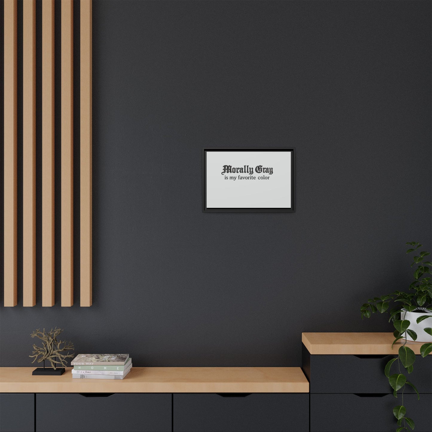 Minimalist black and wood modern interior featuring a framed print with the phrase "Morally Gray is my favorite color" centered on a dark gray wall, styled with greenery and books, Unknown Product.