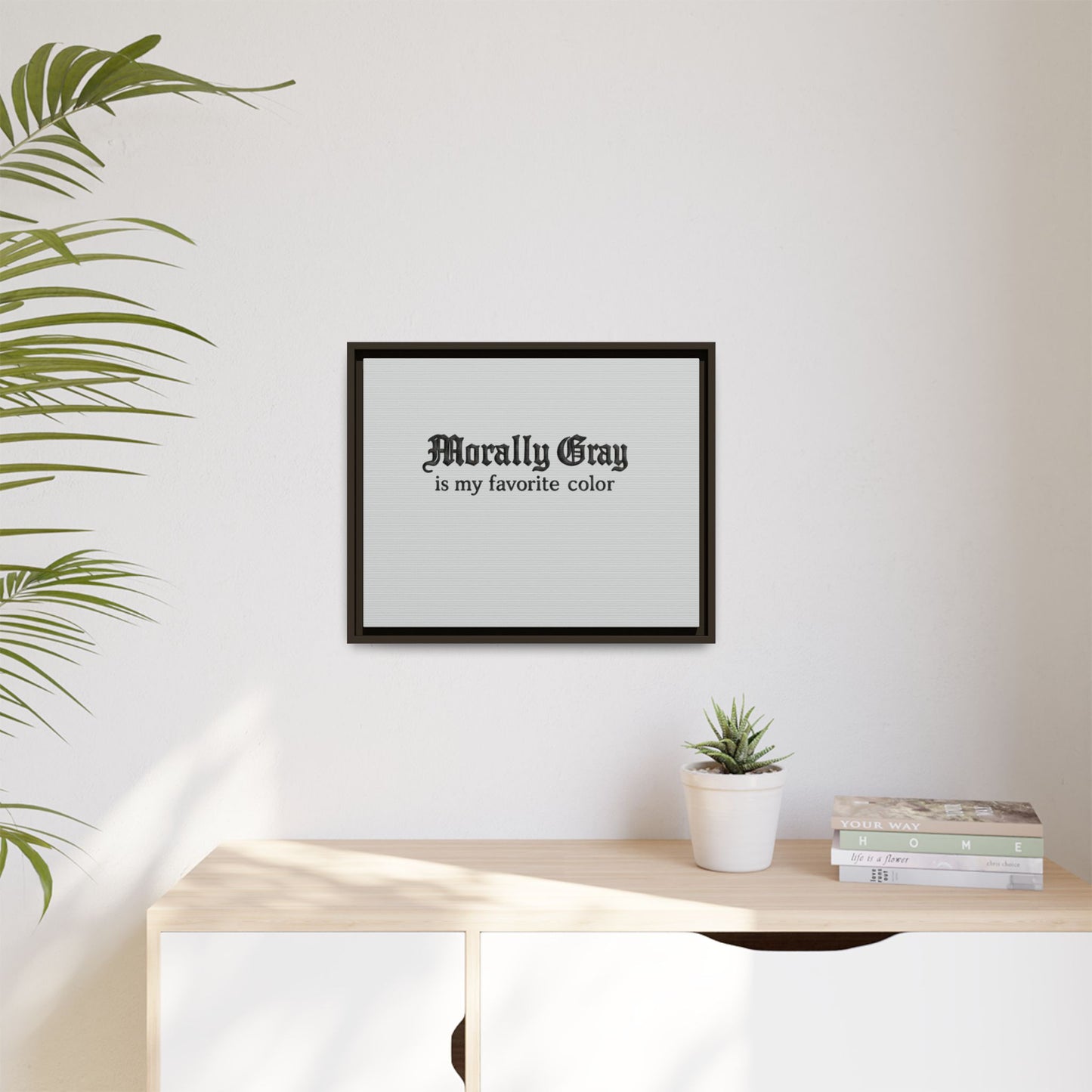 Minimalist framed wall art with black text reading "Morally Gray is my favorite color" displayed above a light wood dresser with a small potted plant and stacked books, featuring the Unknown Product.