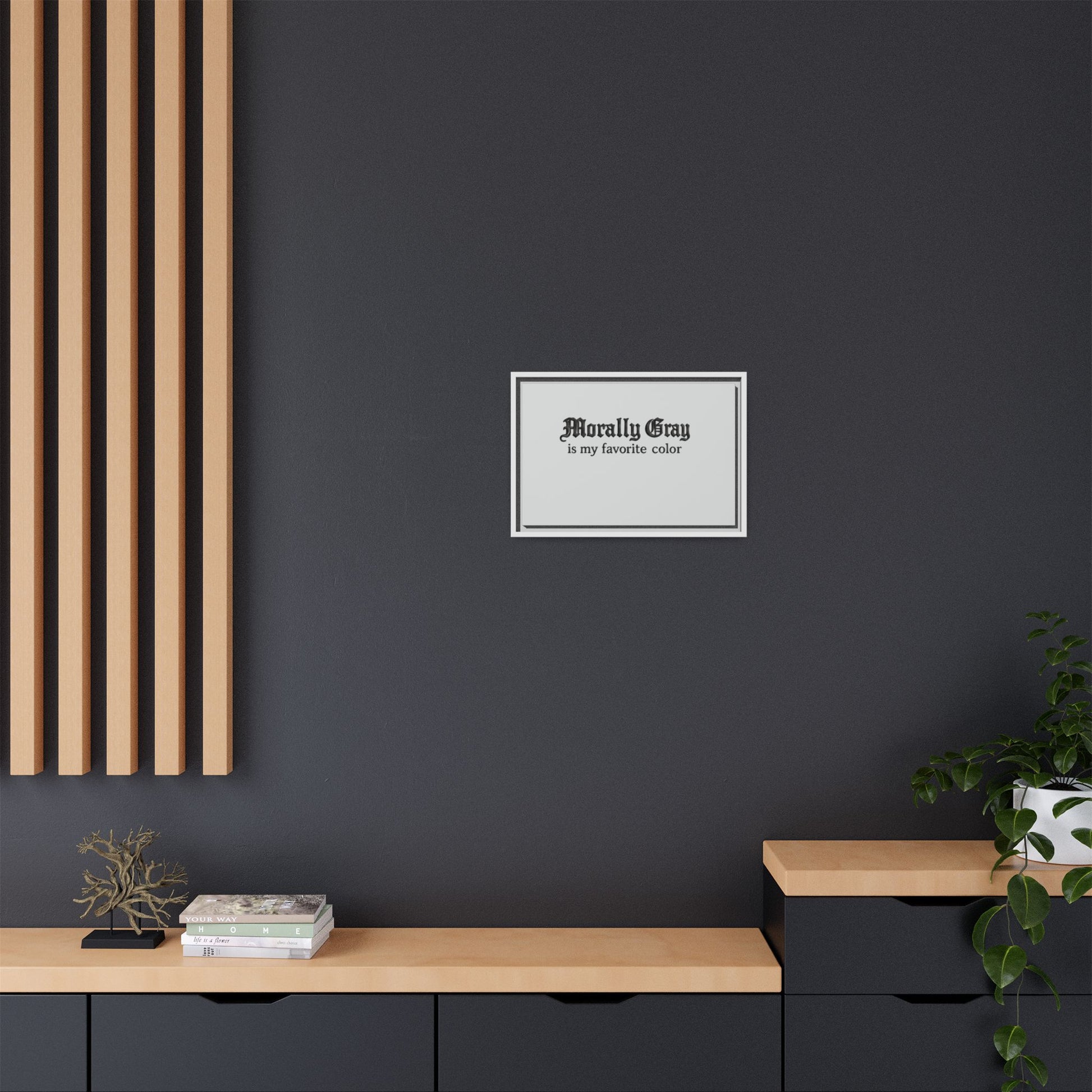 Minimalist room interior with a dark gray wall featuring a framed print that reads "Morally Gray is my favorite color," alongside light wooden shelves and green plants, showcasing Unknown Product.