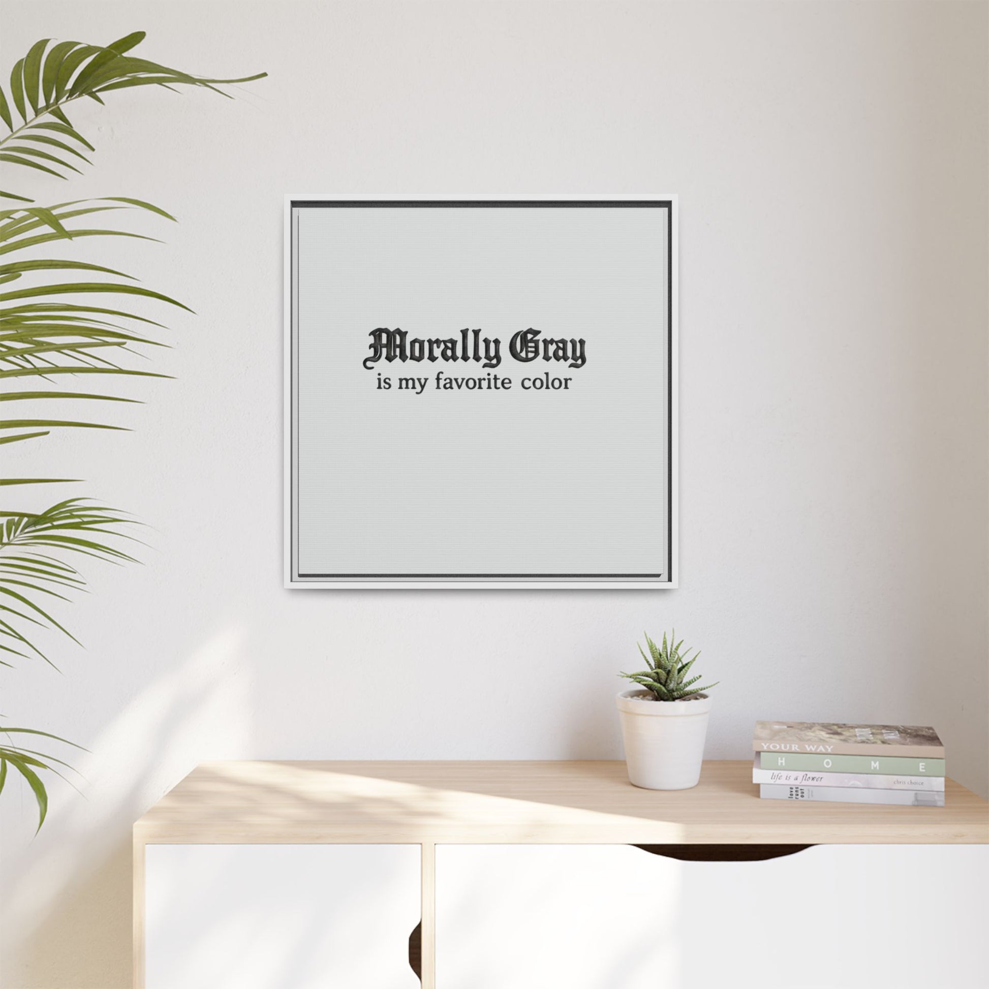 Minimalist wall art with the phrase "Morally Gray is my favorite color" in gothic font above a wooden surface, featuring a small potted plant and stacked books, showcasing Unknown Product.